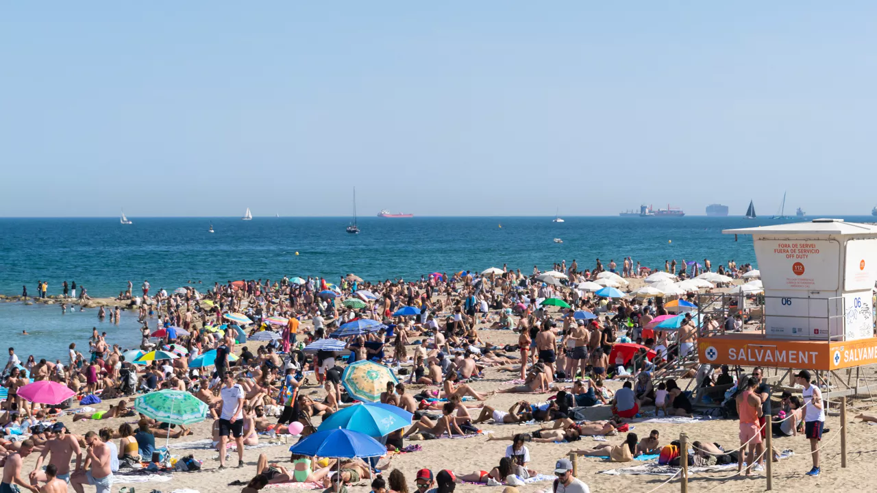 Een strandbeeld! Blauw water, parasols, veel halfnaakte mensen, dabberend in het zand.